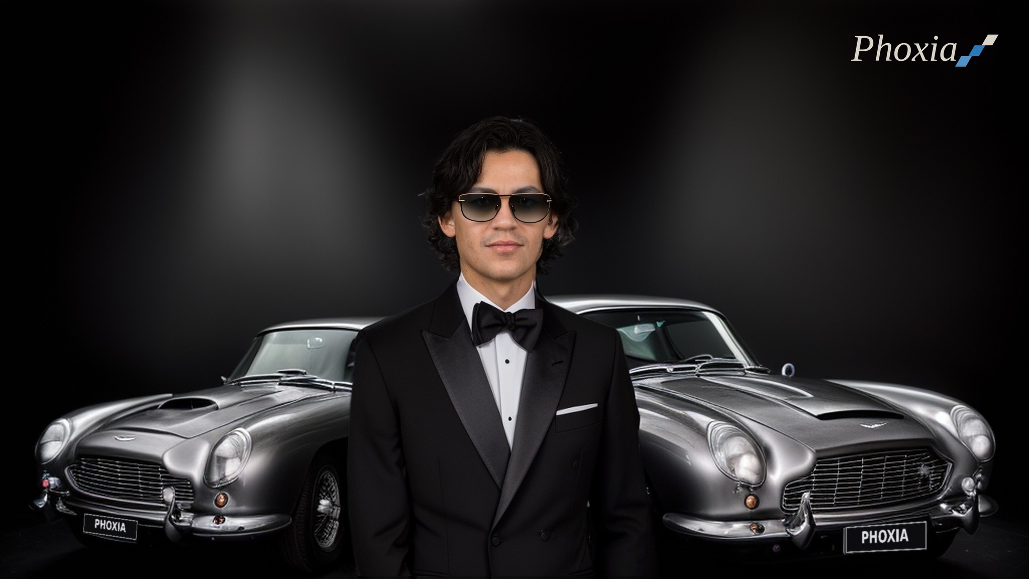 Mathieu Barthélémy en smoking et lunettes de soleil devant deux Aston Martin DB5